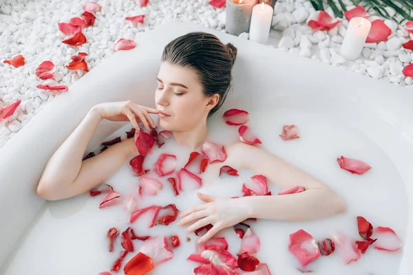 若い女性の泡風呂で横になっているバラの花びらとキャンドルの装飾が燃焼 — ストック写真