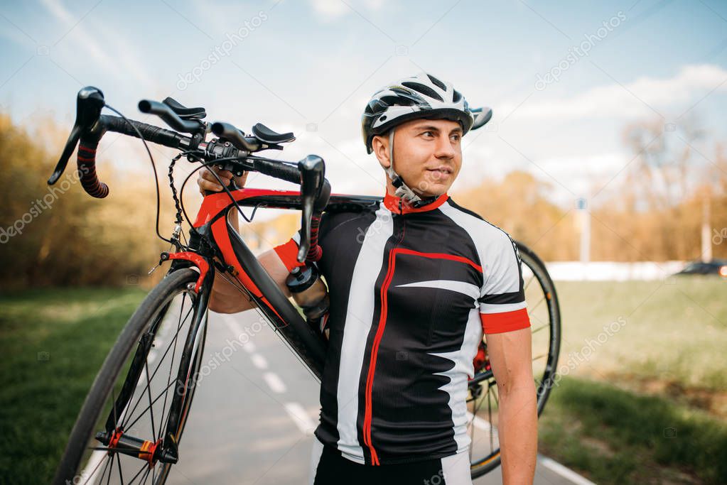 cyclist in helmet and sportswear keeps the bike on shoulder after biking on asphalt road
