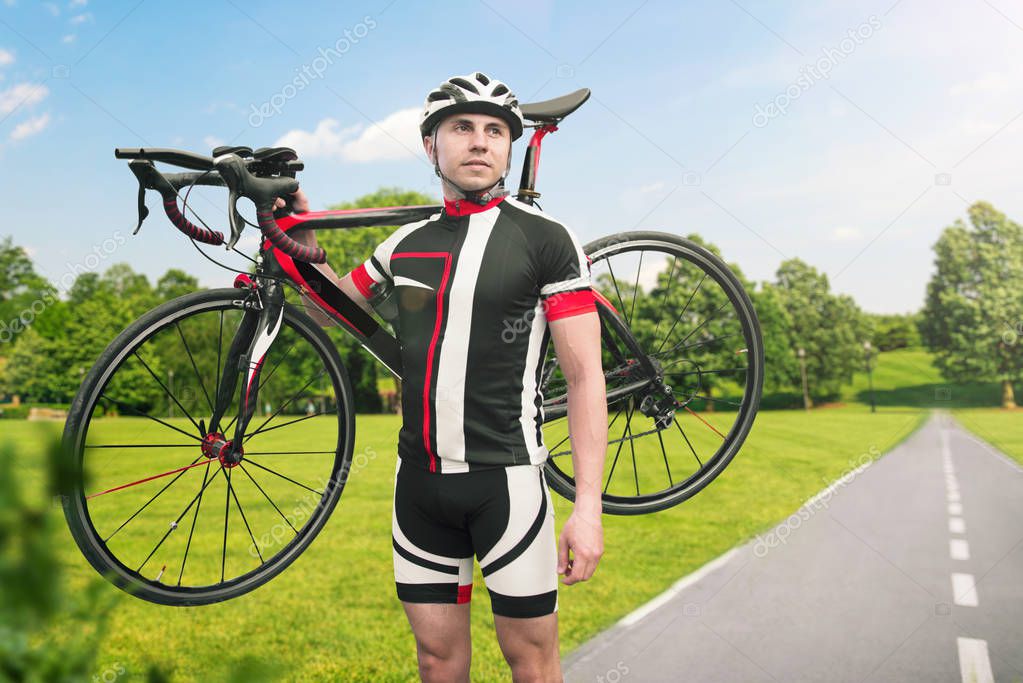 Bycyclist in helmet and sportswear keeps the bike on shoulder after biking on asphalt road. Male sportsman rides on bicycle. Workout on bike path