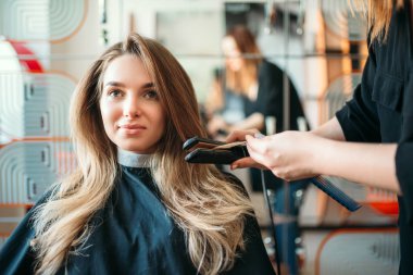 Kuaför saç demirle, kuaförlük salonda kadın müşteri düzeltiyor. Saç modeli yapımı Güzellik Studio, Kuaför saç modeli yapmak
