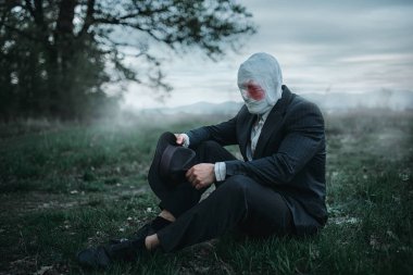 Yüzü kanlı bandaj orman, çılgın katil kavramı, psikopat katil yere oturmuş sarılı olan seri manyak