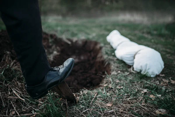 男性杀人犯用铲子挖坟墓为受害者 身体裹在画布上 连环疯子的概念 — 图库照片