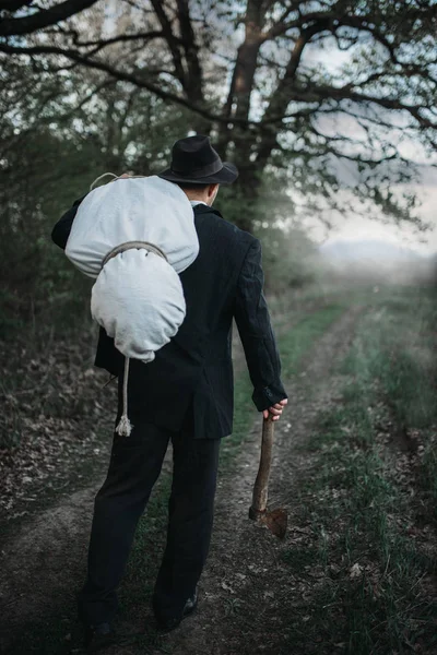 Avcı bir balta ile kurbanın cesedini ormana, seri manyak kavramı bir tuval sarılı taşır