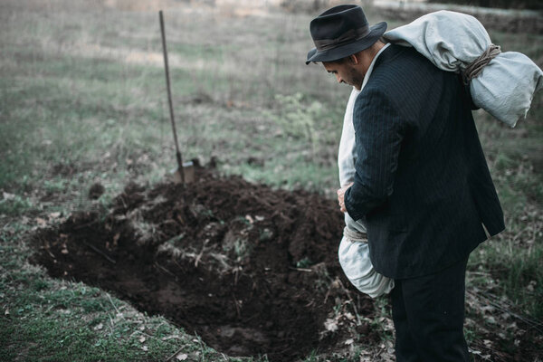 Маньяк бросает окровавленное тело жертвы завернутое в холст в могилу, концепцию серийного убийцы, ужас преступления
