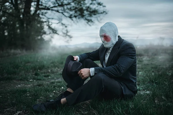 Yüzü kanlı bandaj orman, çılgın katil kavramı, psikopat katil yere oturmuş sarılı olan seri manyak