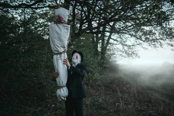 Seri manyak bir tuval üzerine bir ağaç, çılgın katil kavramı, psikopat katil sarılı kurbanın sallanmaktadır