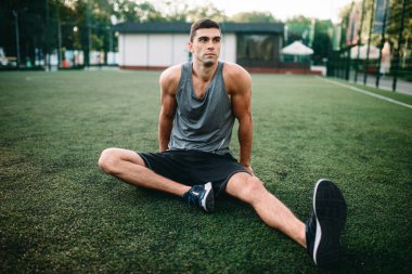 Erkek atlet açık fitness egzersiz üzerinde. Sporcu çim ve germe egzersiz yapıyor üzerinde oturur
