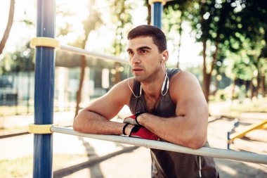 Erkek atlet kulaklık yatay bar, açık alan fitness egzersiz üzerinde poz veriyor. Güçlü sporcu spor eğitim Parkı