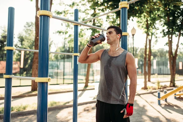 男运动员在耳机饮水后进行户外健身训练 强的运动员在体育锻炼在夏天公园 — 图库照片