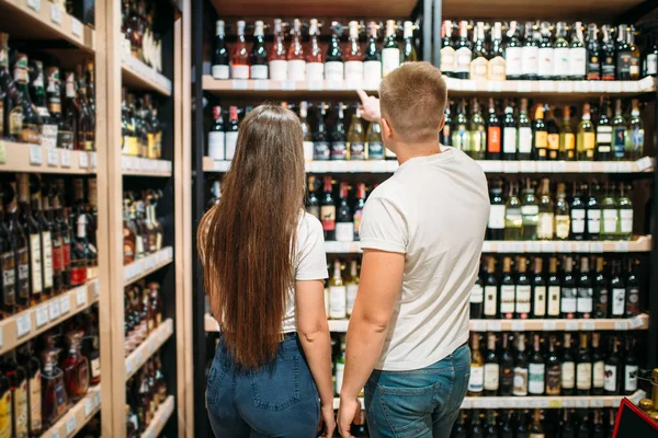年轻夫妇在酒精市场寻找葡萄酒 背景瓶子货架 — 图库照片