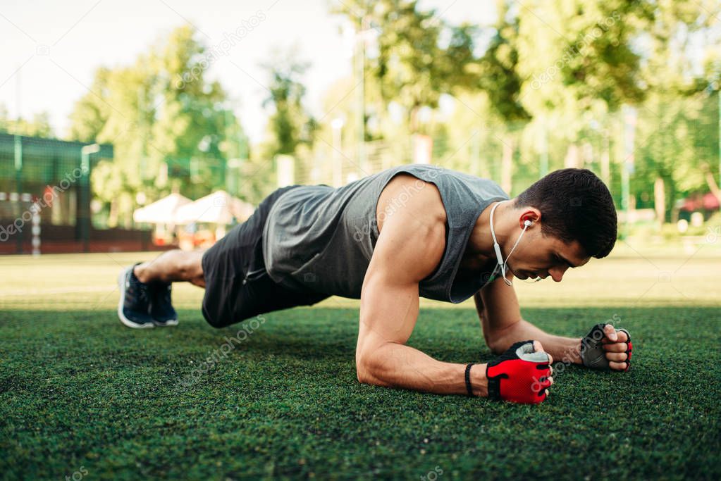 Athletic man doing push-up exercise on a grass, outdoor fitness workout. Muscular sportsman on sport training in summer park