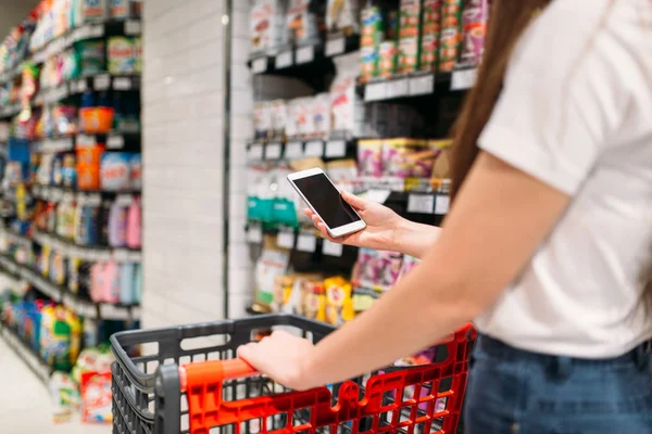 Female customer with phone in hand, food store. Woman uses smartphone in grocery