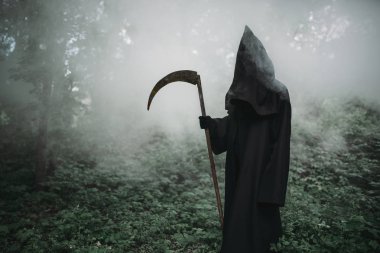 Ölüm bir siyah hoodie ve karanlık sisli ormanın içinde bir tırpan ile. Korku tarzı, korku, ürkünç iblis
