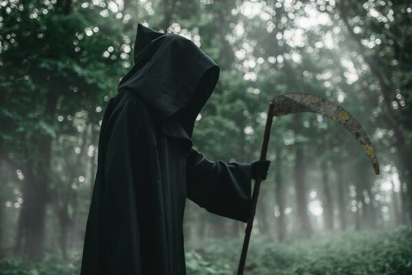 Death in a black hoodie and with a scythe in forest. Horror style, fear, spooky evil