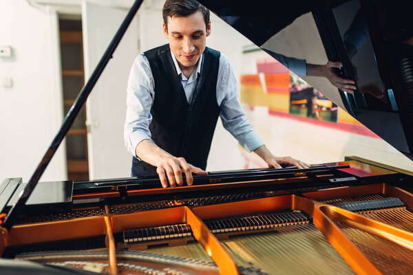 Male pianist sets the grand piano before the performance of a musical composition. Musician adjusts royale, classical musical instrument tuning