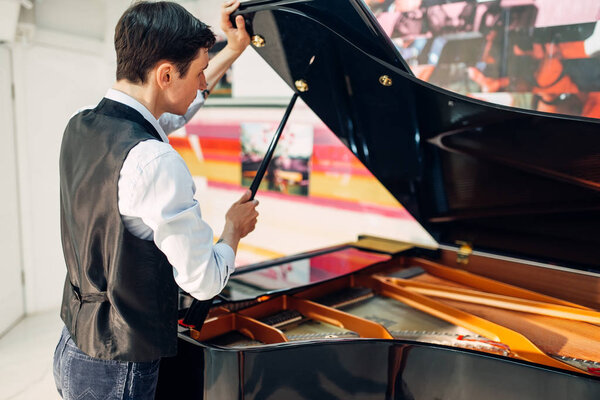 Male pianist opens the lid of the black grand piano. Musician adjusts royale, classical musical instrument tuning