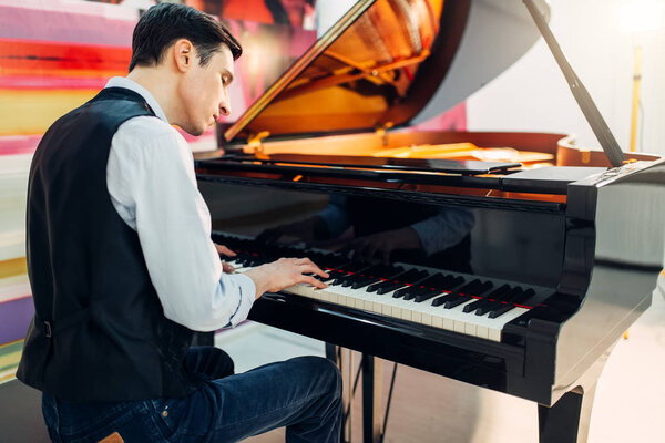 Male pianist at the classical black grand piano, performance in studio. Musician plays melody at the royale keyboard, musical instrument