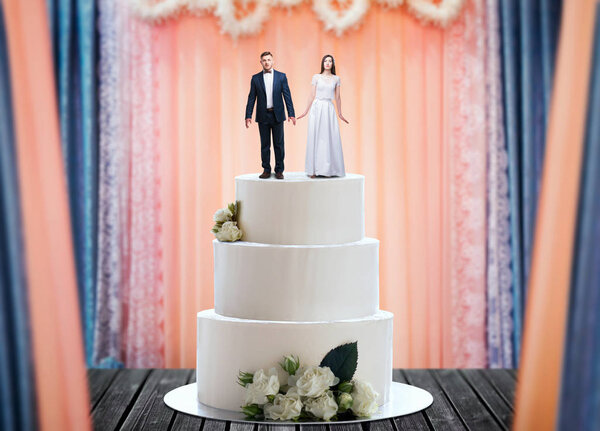 Wedding cake with bride and groom figures on the top, marriage proposal. Sweet pie for newlyweds with little figurines