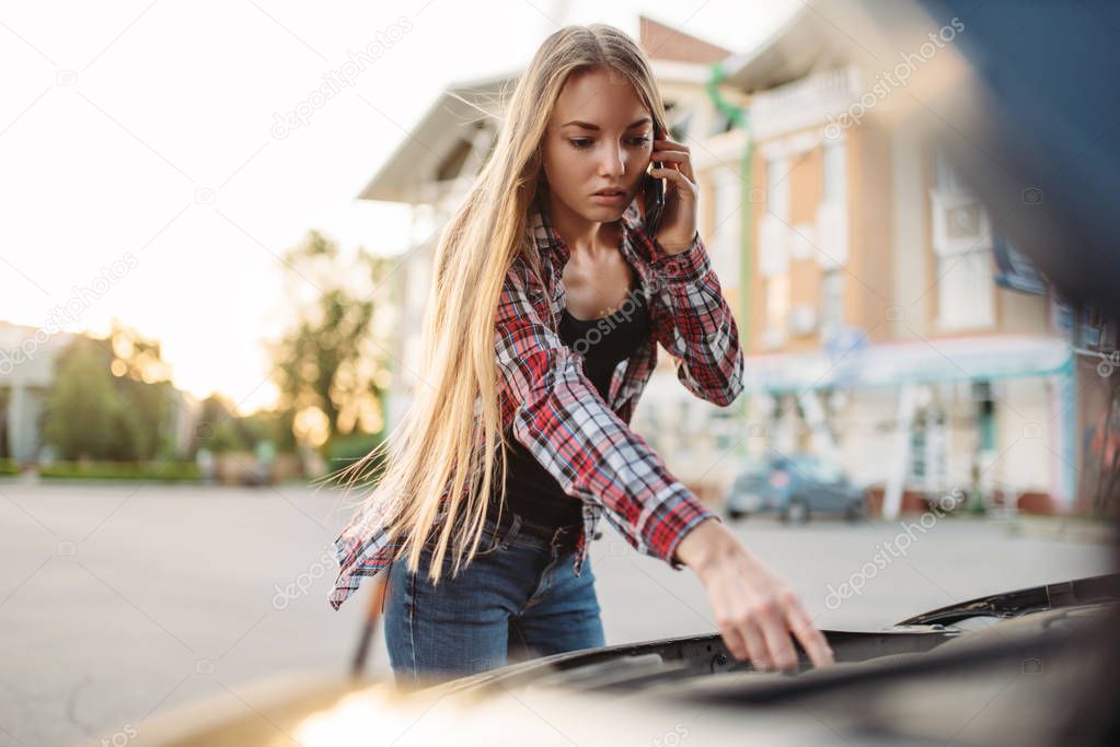 Car breakdown concept, sad woman against open bonnet on the roadside. Female driver looks at the broken vehicle engine