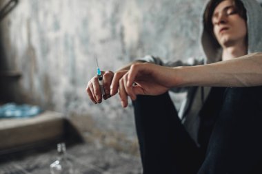 Junkie with syringe in hand sitting on the floor after dose, bottle of alcohol is near. Drug addiction concept, narcotic addicted people clipart