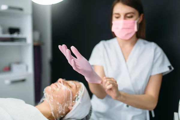 Schoonheidsspecialiste Draagt Handschoenen Tegen Patiënt Met Gezichtsmasker Het Wegwerken Van — Stockfoto