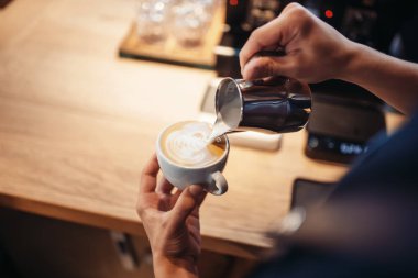 Barista el krem kahve, ahşap masa arka plan üzerine bir fincan içine dökülen. Barmen tarafından profesyonel kapuçino hazırlık