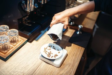 Barista el kahve çekirdekleri plaka ayakta ölçeklerde, ahşap arka plan tezgaha içine dökülen. Profesyonel espresso hazırlık kafeterya barmen tarafından