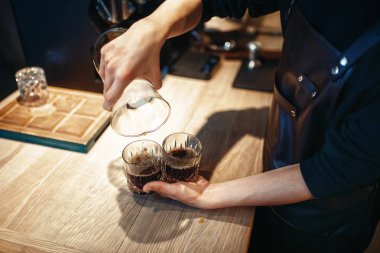 Genç erkek barista kafe tezgahta taze siyah kahve yapıyor. Barmen kafeteryada çalışıyor, barmen espresso hazırlar