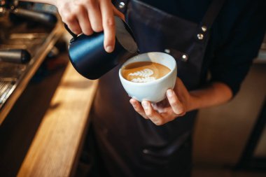Barista el krem kahve, ahşap masa arka plan üzerine bir fincan içine dökülen. Barmen tarafından profesyonel kapuçino hazırlık