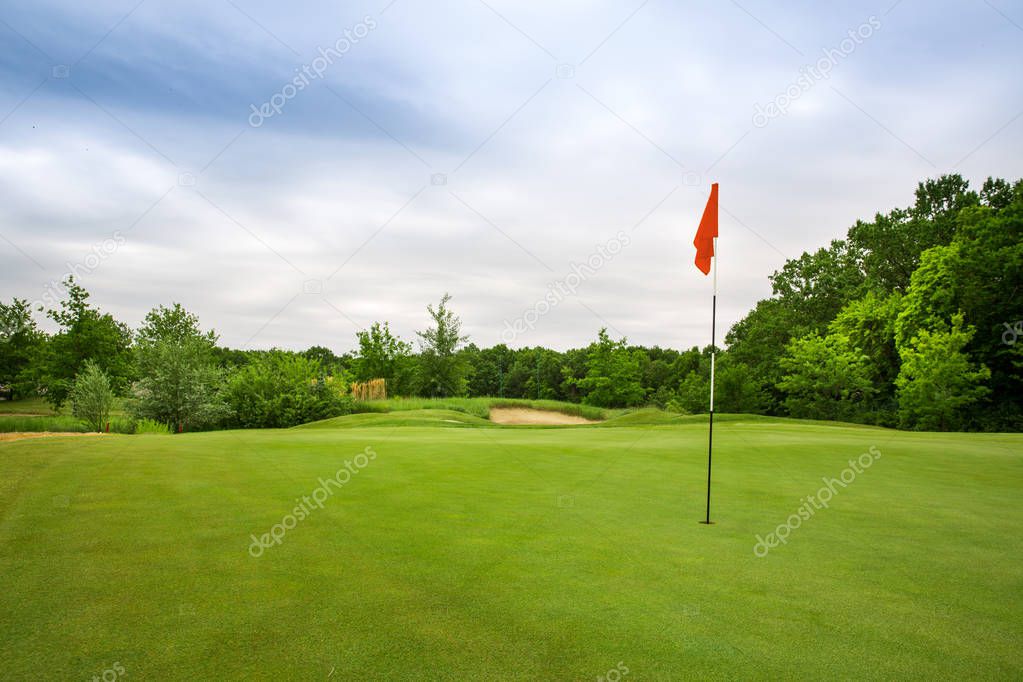 Final hole with flag, lawn with green trimmed grass on golf course, nobody. Meadow in sport club, empty playground for golfing