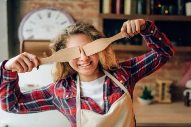 Apronda oynak ev kadını onun tahta spatula gözlerle, mutfak iç arka plan üzerinde kapsar. Sağlıklı vejetaryen yemek, yapım mutlu kadın aşçı yemek salata