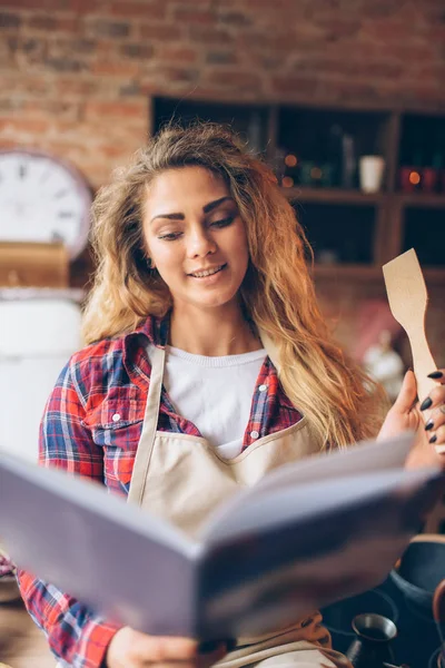 Apronda Genç Kadını Tarif Kitabı Mutfak Arka Plan Üzerinde Okur — Stok fotoğraf