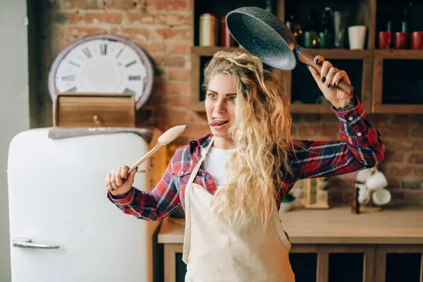 キッチン インテリアの背景には フライパン 木のへらを手で保持なエプロンで主婦を笑っています ヘルシーなベジタリアン料理を作る女性料理サラダ料理 — ストック写真
