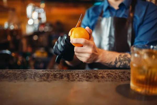 バーでオレンジを剥離エプロンで男性バーテンダー カウンター アルコール飲料の準備 バーテンダーの職業 — ストック写真