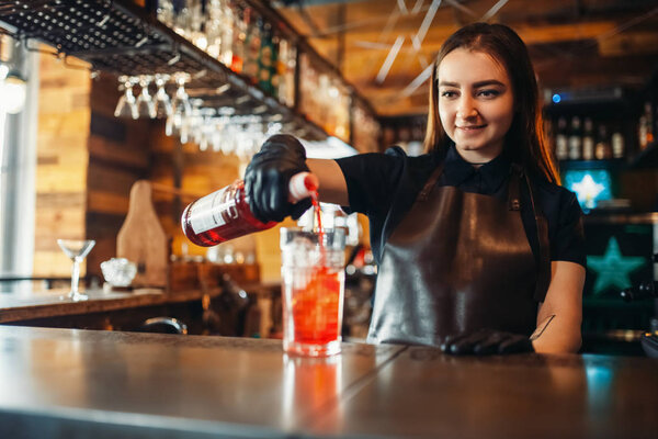 Female barman prepares alcoholic coctail with ice. Alcohol drink preparation. Woman bartender working at the bar counter in pub