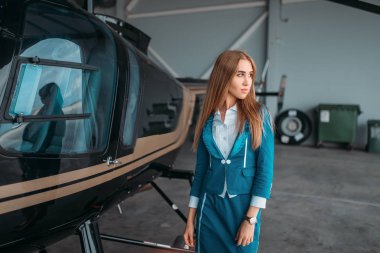 Hostes elbiseli helikopter hangarda karşı teşkil etmektedir. Helikopter yakınındaki üniformalı hostes. Özel havayolu