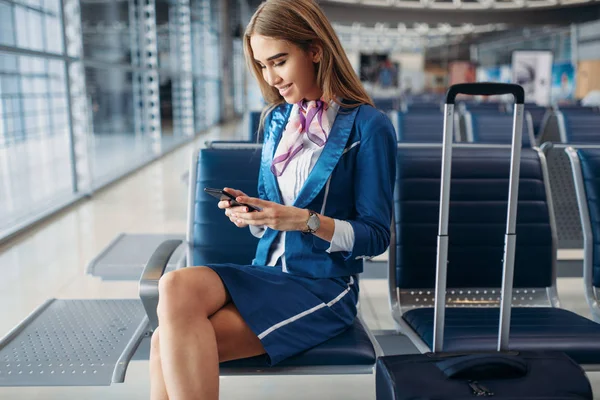空姐坐在机场等候区的座位上 使用手机 带行李的空姐 带手提行李的空姐 — 图库照片
