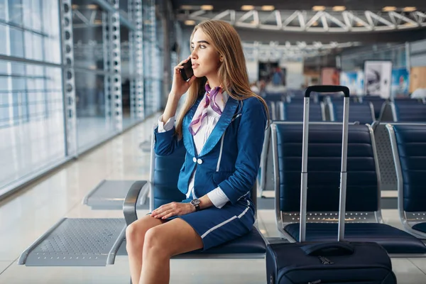 Stewardessa Walizką Siedząc Siedzeniu Poczekalni Lotnisku Rozmawia Przez Telefon Komórkowy — Zdjęcie stockowe