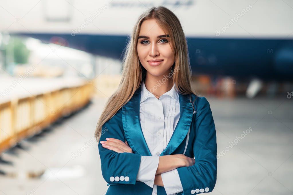 Attractive stewardess in uniform poses against airport building. Air hostess in suit near terminal. Flight attendant occupation