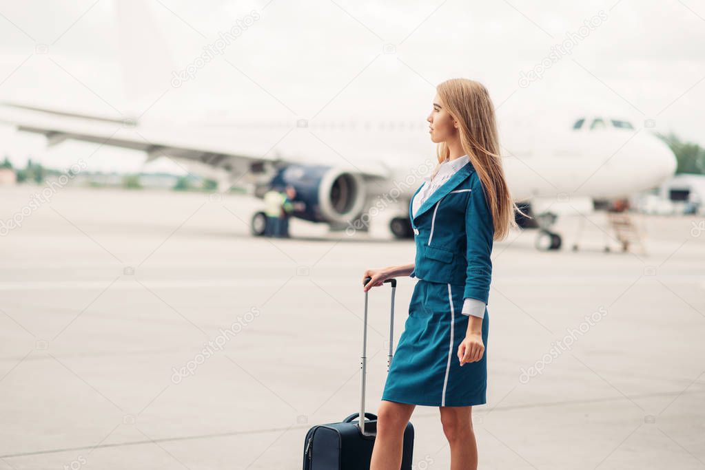 Sexy stewardess with suitcase on aircraft parking,  airplane on background.