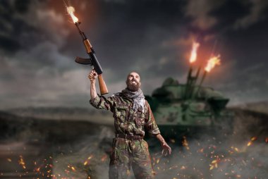 Bearded terrorist with rifle in hands stands in explosion and fire. Terrorism and terror, soldier in khaki camouflage clipart