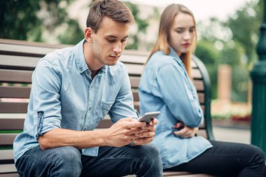 Bağımlılık, parkta bankta genç çift telefon. Erkek ve kadın kullanarak onların akıllı telefonlar, bağımlısı insanlar