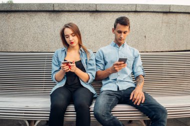 Bağımlılık, parkta bankta genç çift telefon. Erkek ve kadın kullanarak onların akıllı telefonlar, bağımlısı insanlar