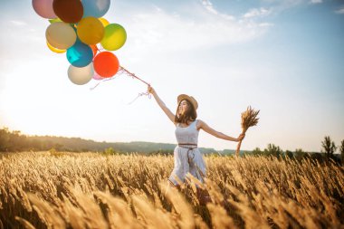 Buğday alanında yürüyüş renkli hava balonları kızla. Güneşli bir gün, yaz çayır üzerinde güzel kadın