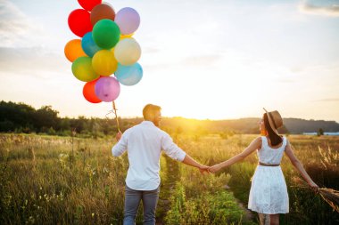 Mutlu çift demet balonlar ve buğday alanında öpüşme tutar. Güzel çift eğlence yaz çayır üzerinde