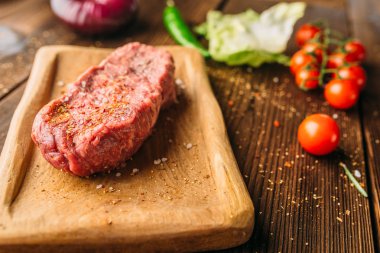 Suyu parça baharat biftek ve ahşap masa portre, taze sebze kimse. Pişmemiş beefstek, biber ve bitki, gıda hazırlama, pişirme