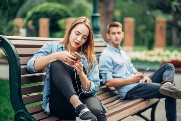 电话成瘾 在公园的长凳上微笑的情侣 男人和女人使用他们的智能手机 社会成瘾的人 — 图库照片