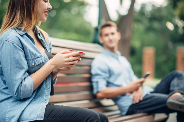 电话成瘾 在公园的长凳上微笑的情侣 男人和女人使用他们的智能手机 社会成瘾的人 — 图库照片