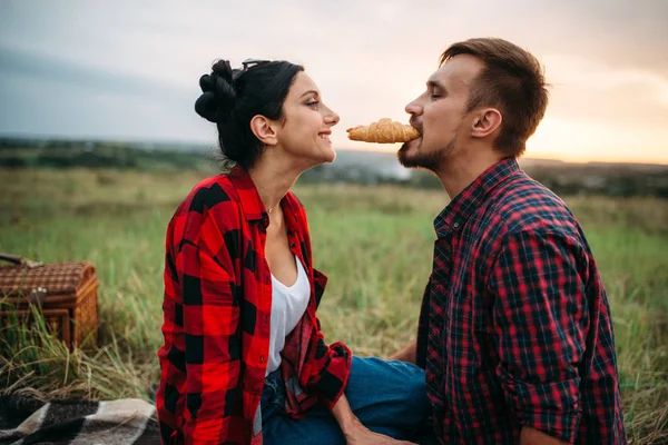 幸せな愛のカップルは 夏の畑でピクニックにクロワッサンを食べるします 男と女のロマンチックな視察旅行 — ストック写真