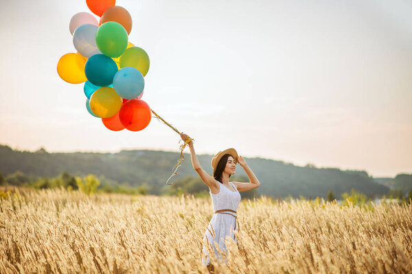 Girl with colorful air balloons in a rye field. Pretty woman on summer meadow